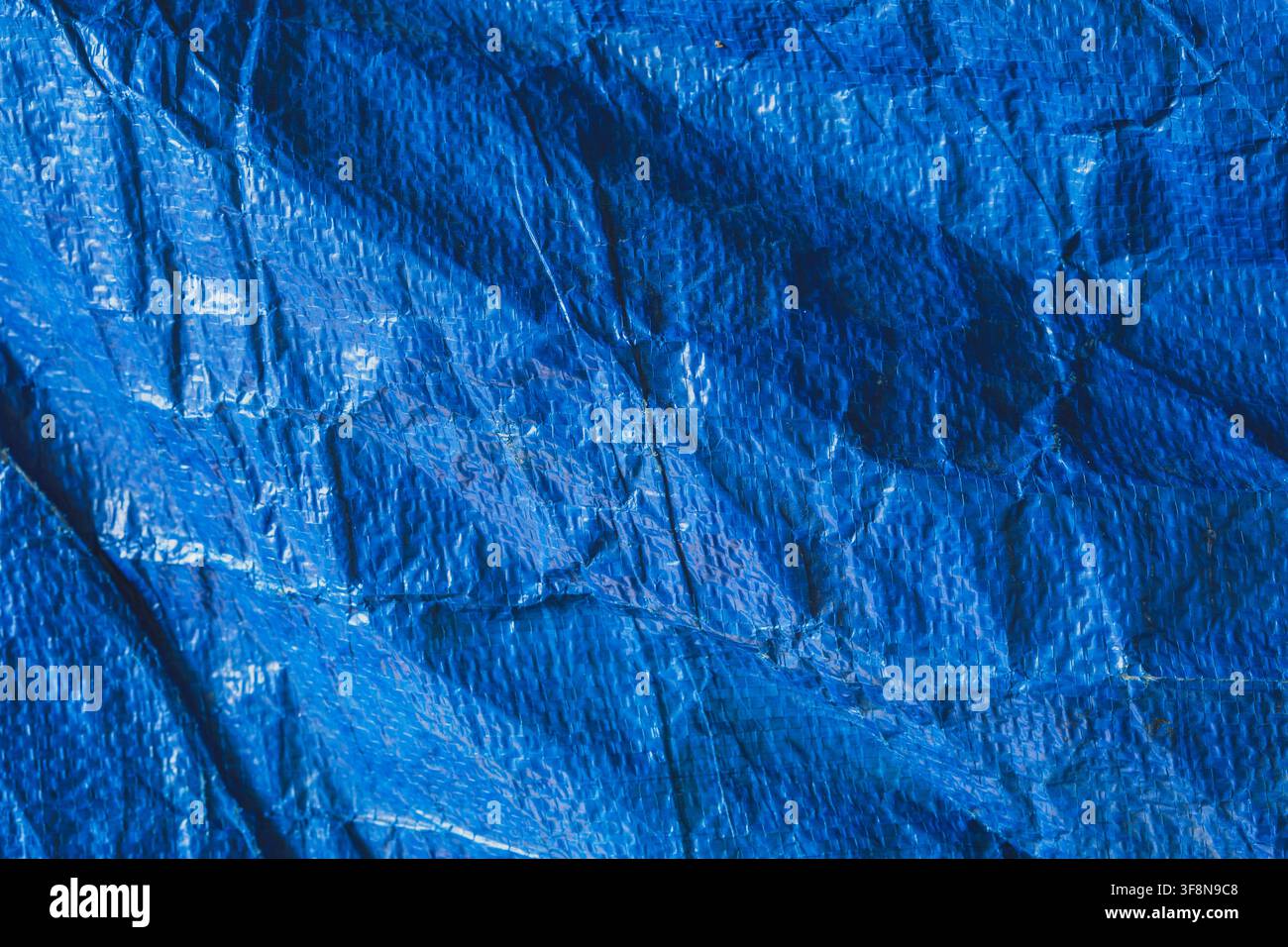 Close up background texture of a wrinkled blue plastic tarp with a woven pattern. Stock Photo