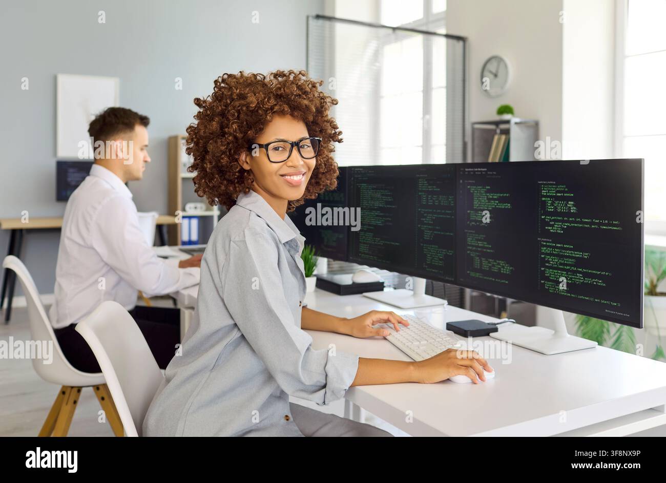 Smiling woman programmer working on code at desktop in bright tech office Stock Photo