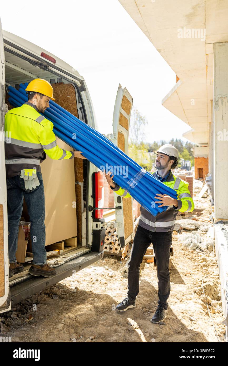 Two builders in high visibility jackets unloading blue pipes Stock Photo