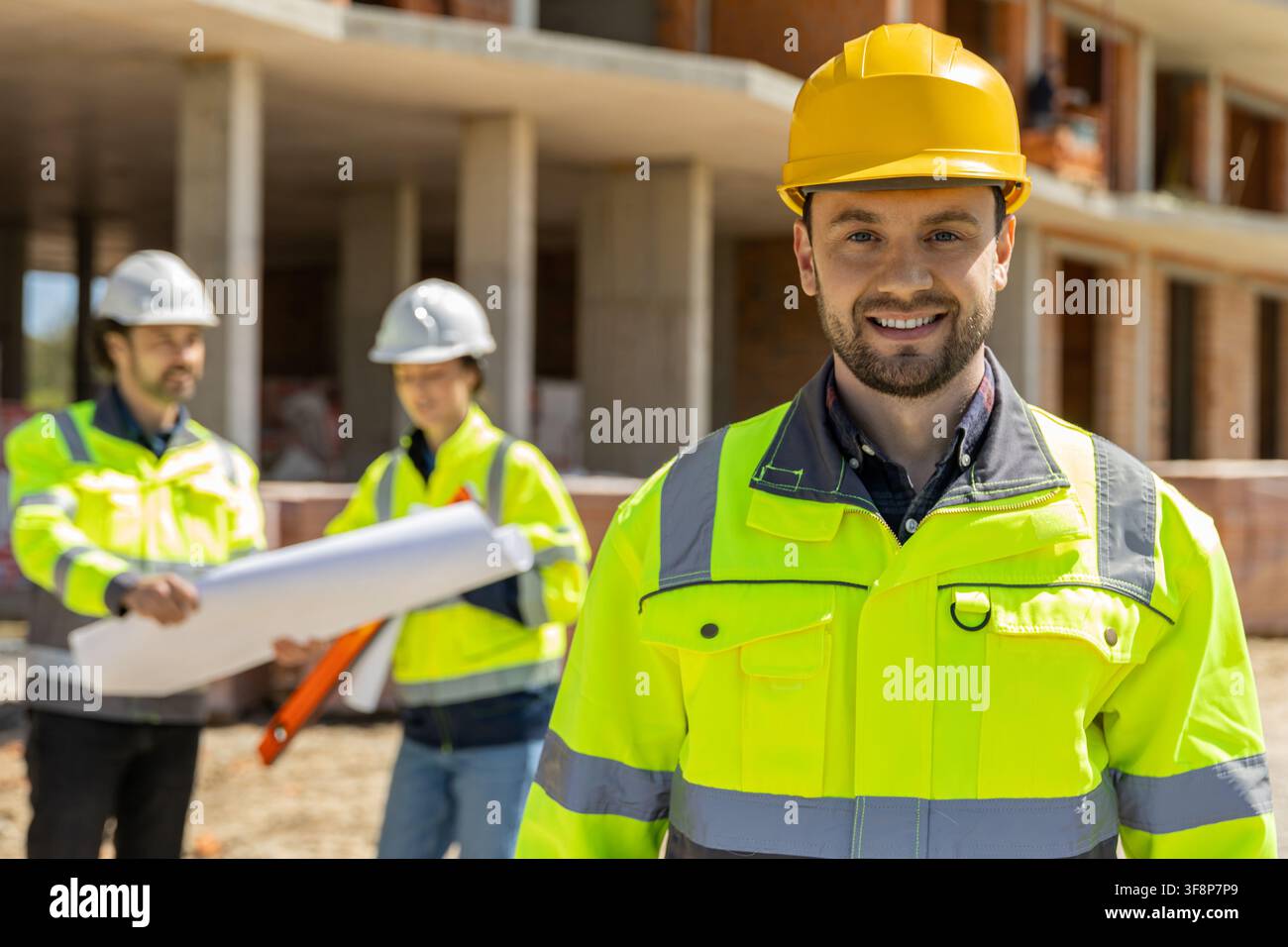 Smiling young builder standing in yellow hardhat Stock Photo