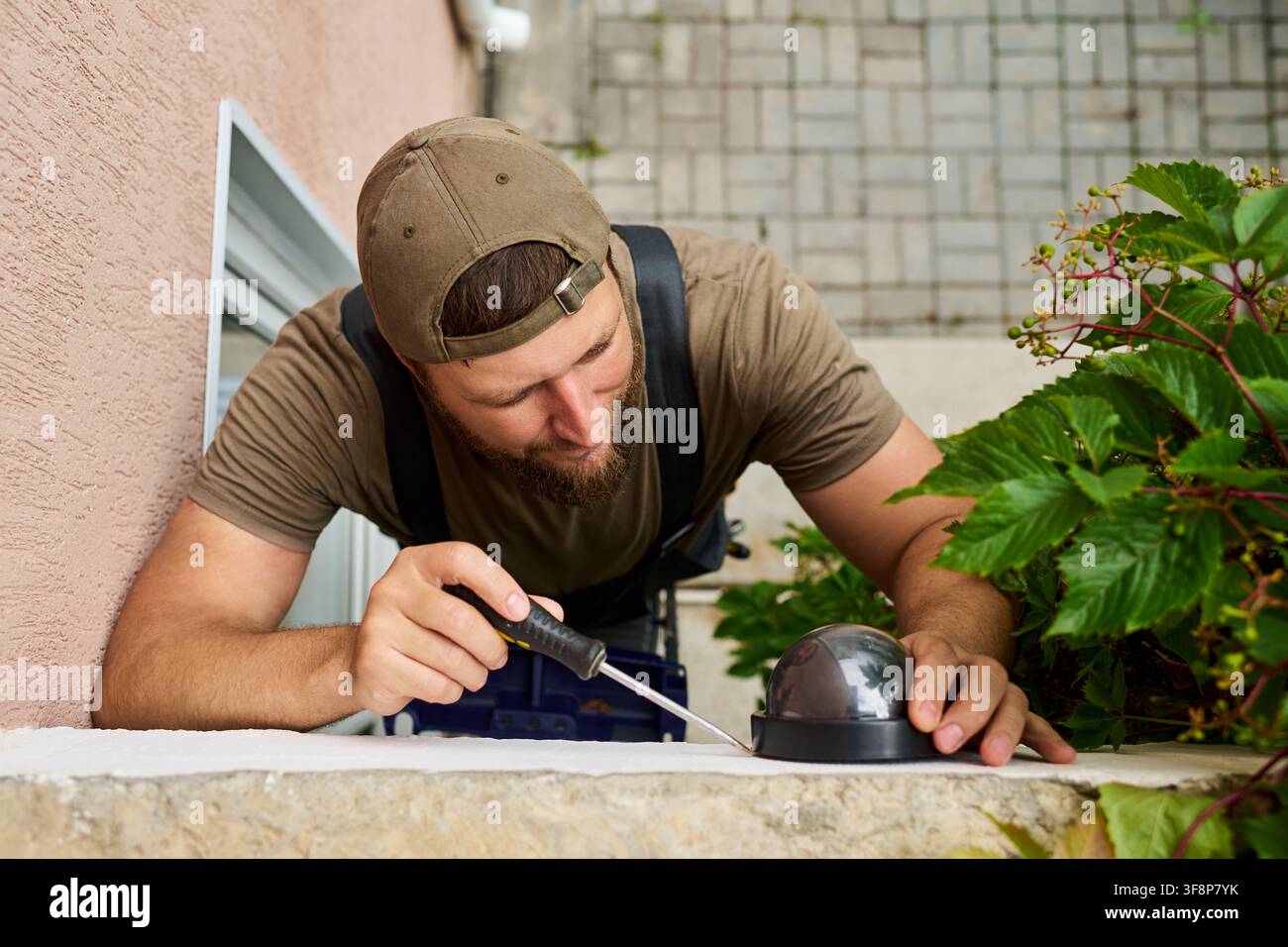Man Installing Security Camera with Screwdriver on Building Wall Stock Photo