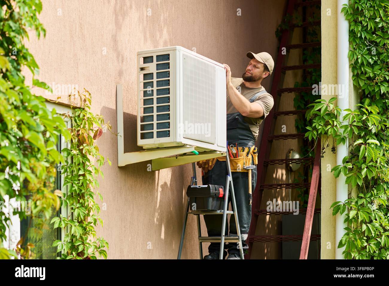 Technician Man Installing Air Conditioner Unit on House Wall Stock Photo