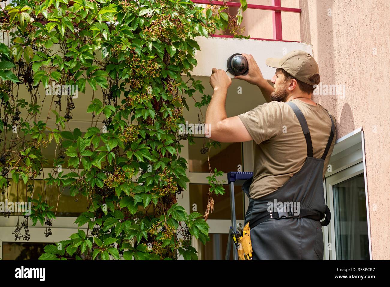 Technician Installing Security Camera on Building Exterior Wall Stock Photo