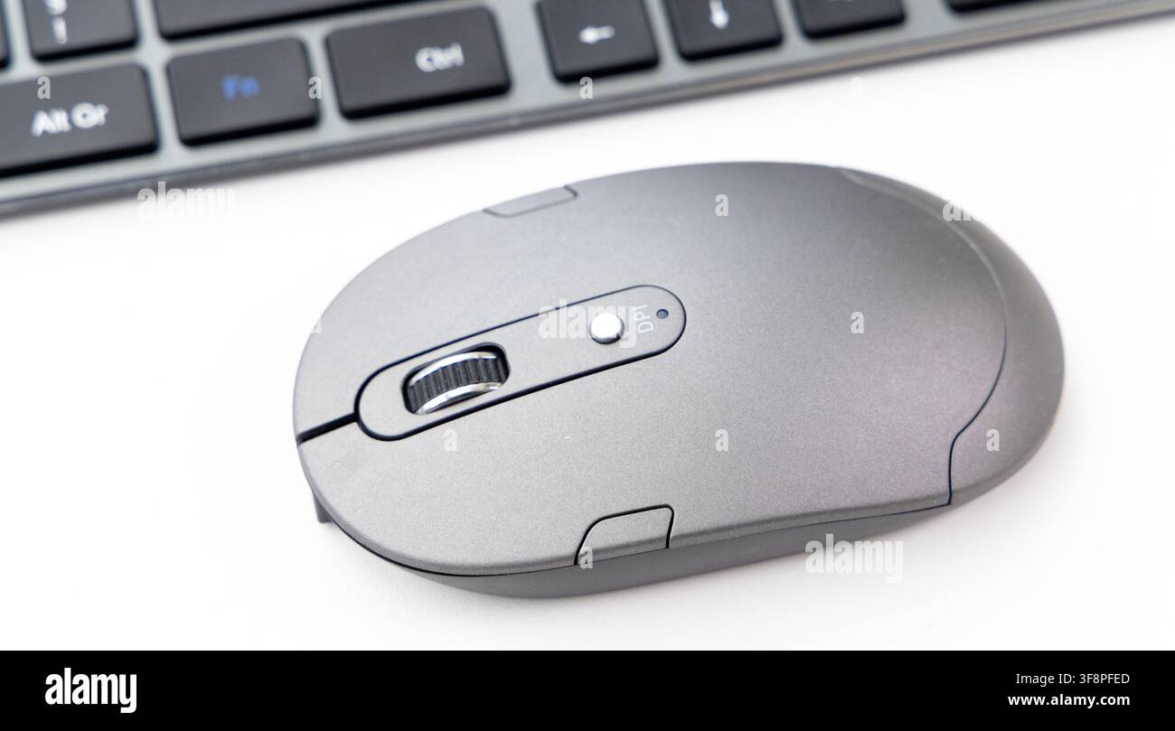 A modern grey wireless computer mouse sits next to a keyboard Stock Photo