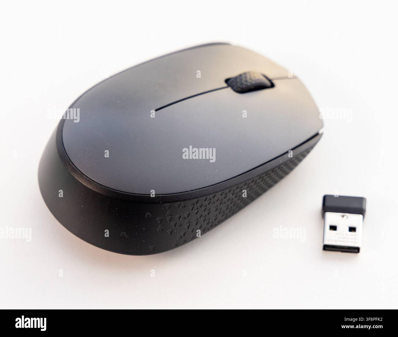 A black wireless computer mouse and its USB receiver sit on white Stock Photo