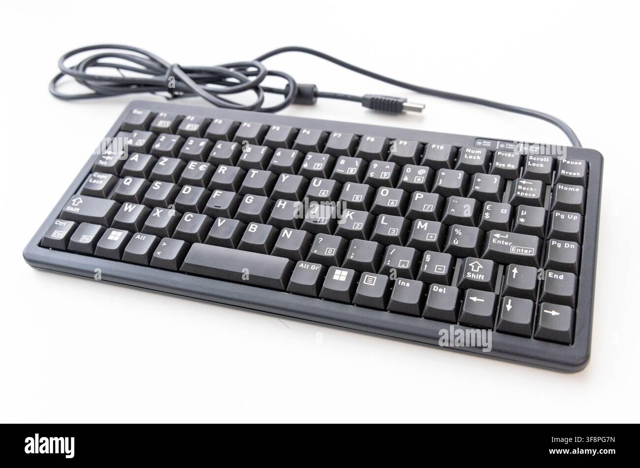 A black wired computer keyboard rests on a plain white surface Stock Photo