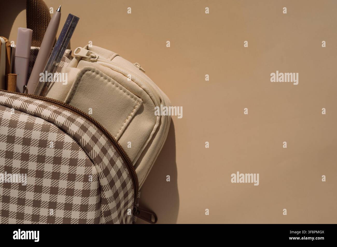 Checkered backpack with stationery and pencil case in warm light, back to school background Stock Photo