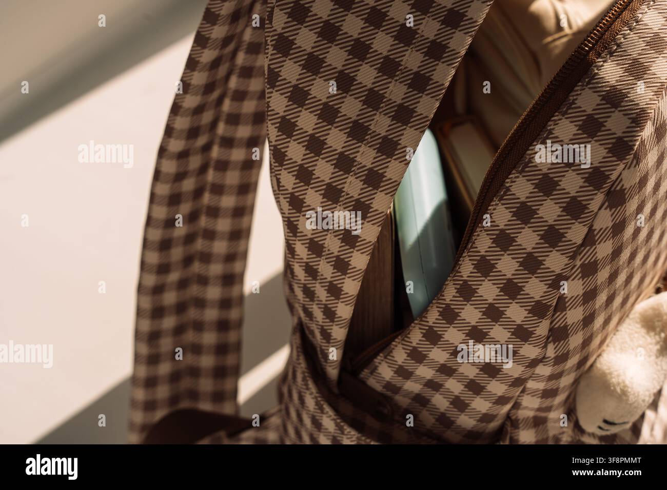 Open checkered backpack with school supplies in dramatic sunlight, back to school concept Stock Photo