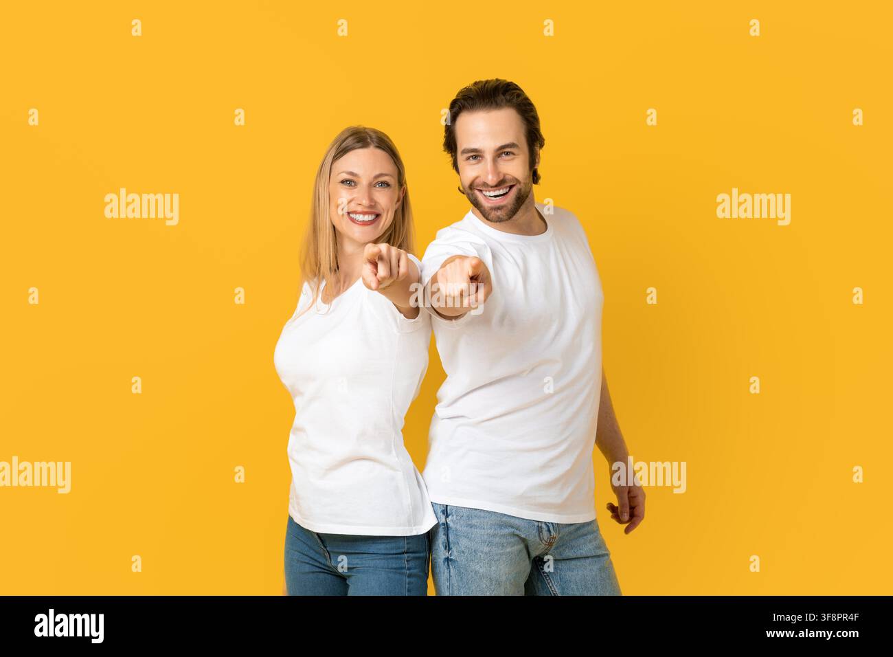 Happy Caucasian Male And Female Pointing Smiling At Camera, Yellow Background, Business Concept Stock Photo