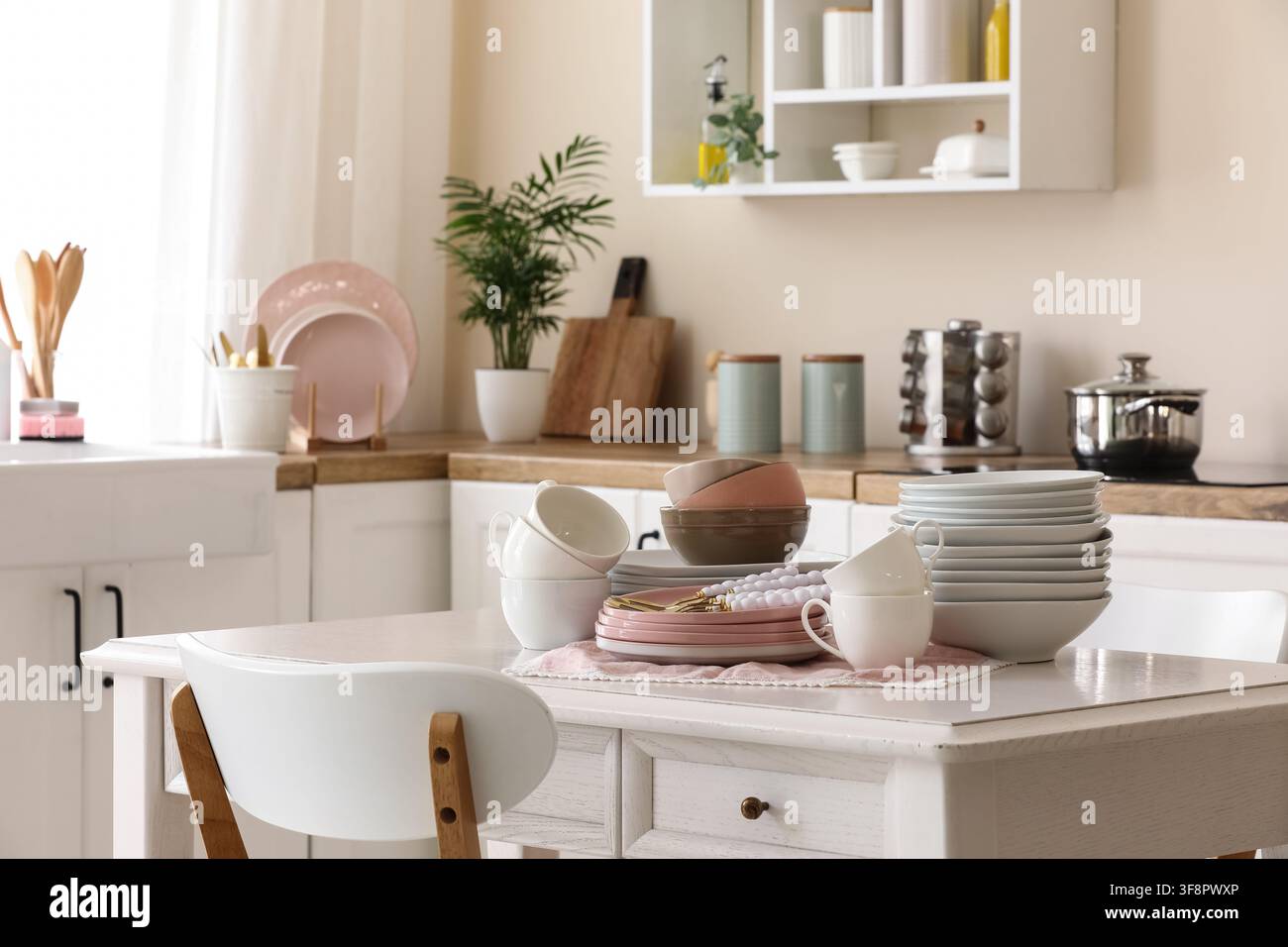 Clean kitchen interior with white dining table, stacked dishes, and modern kitchenware for home living and organization Stock Photo