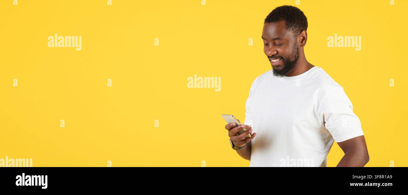 Happy Black Man Using Smartphone, Yellow Background, Technology Concept Stock Photo