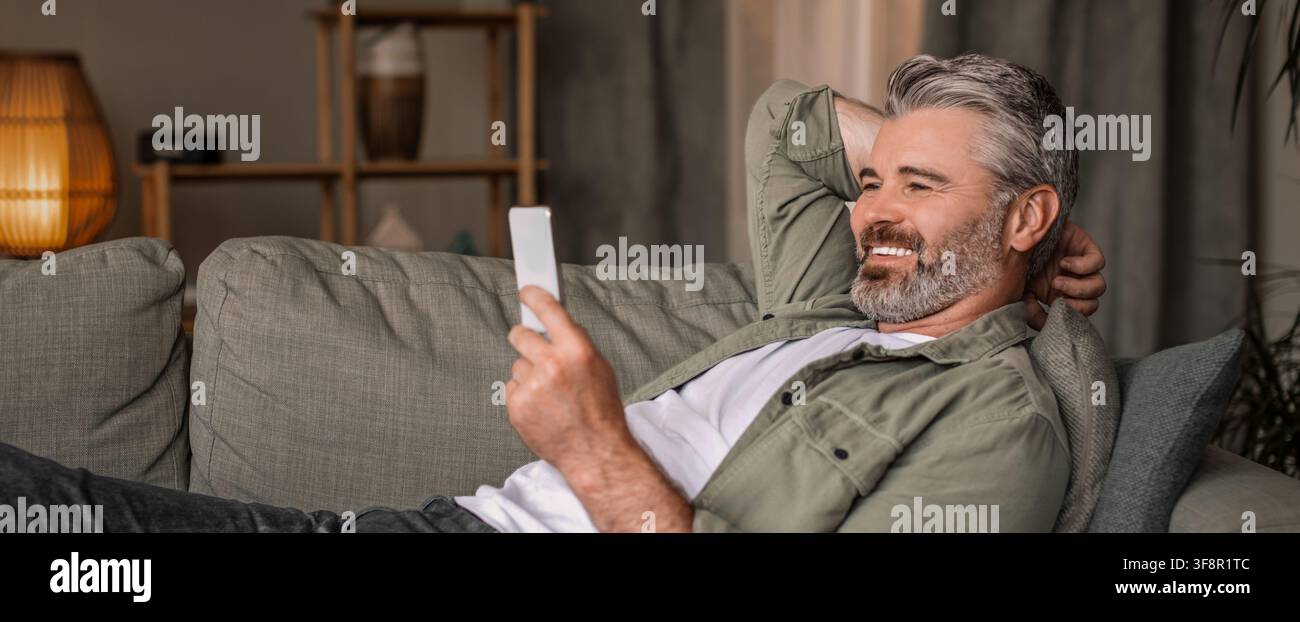 Happy Elderly Caucasian Man Using Smartphone Relaxing At Home, Lifestyle Concept Stock Photo