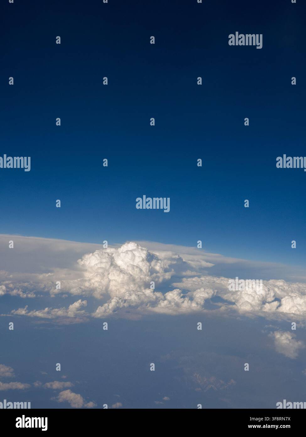 Aerial view of dramatic white cumulus clouds beneath a deep blue sky, photographed through an airplane window at high altitude Stock Photo
