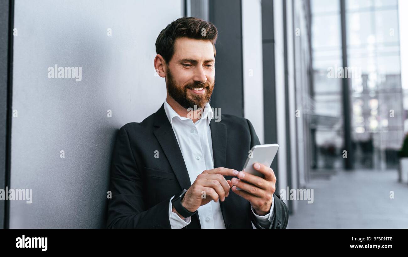 Businessman Smiling While Using Smartphone In Modern Office, Digital Communication Concept Stock Photo