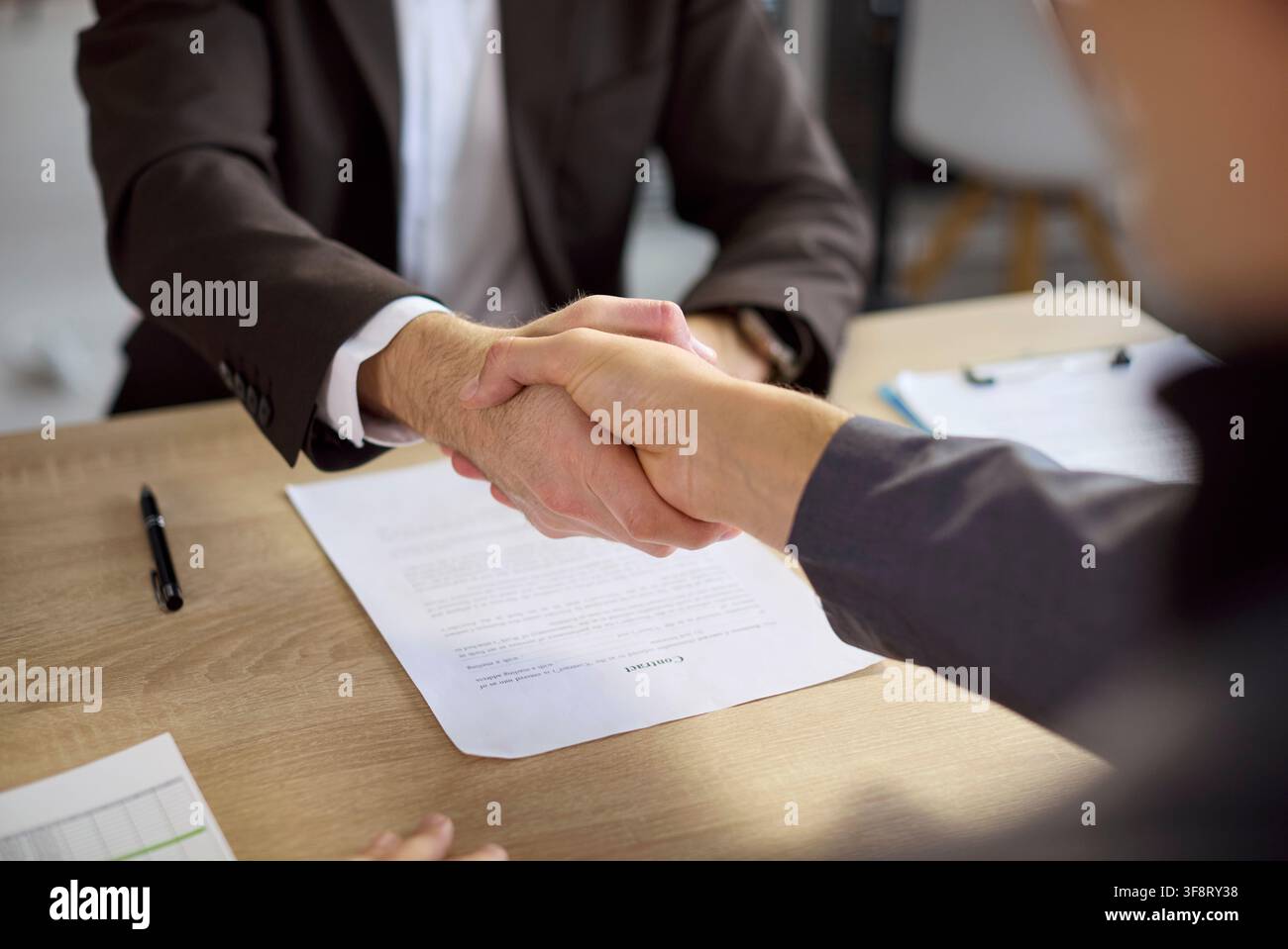 Executives shaking hands over contract documents to finalize a business deal Stock Photo