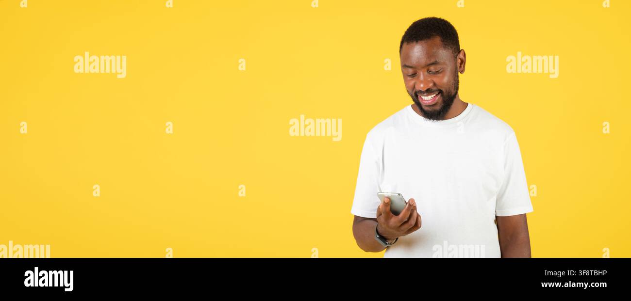 Smiling Black Man Using Smartphone On Yellow Background, Technology Concept Stock Photo