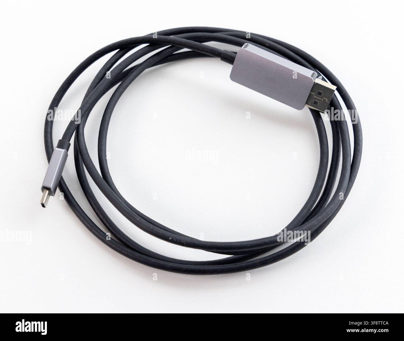 A coiled black data cable with grey connectors rests on a white background Stock Photo
