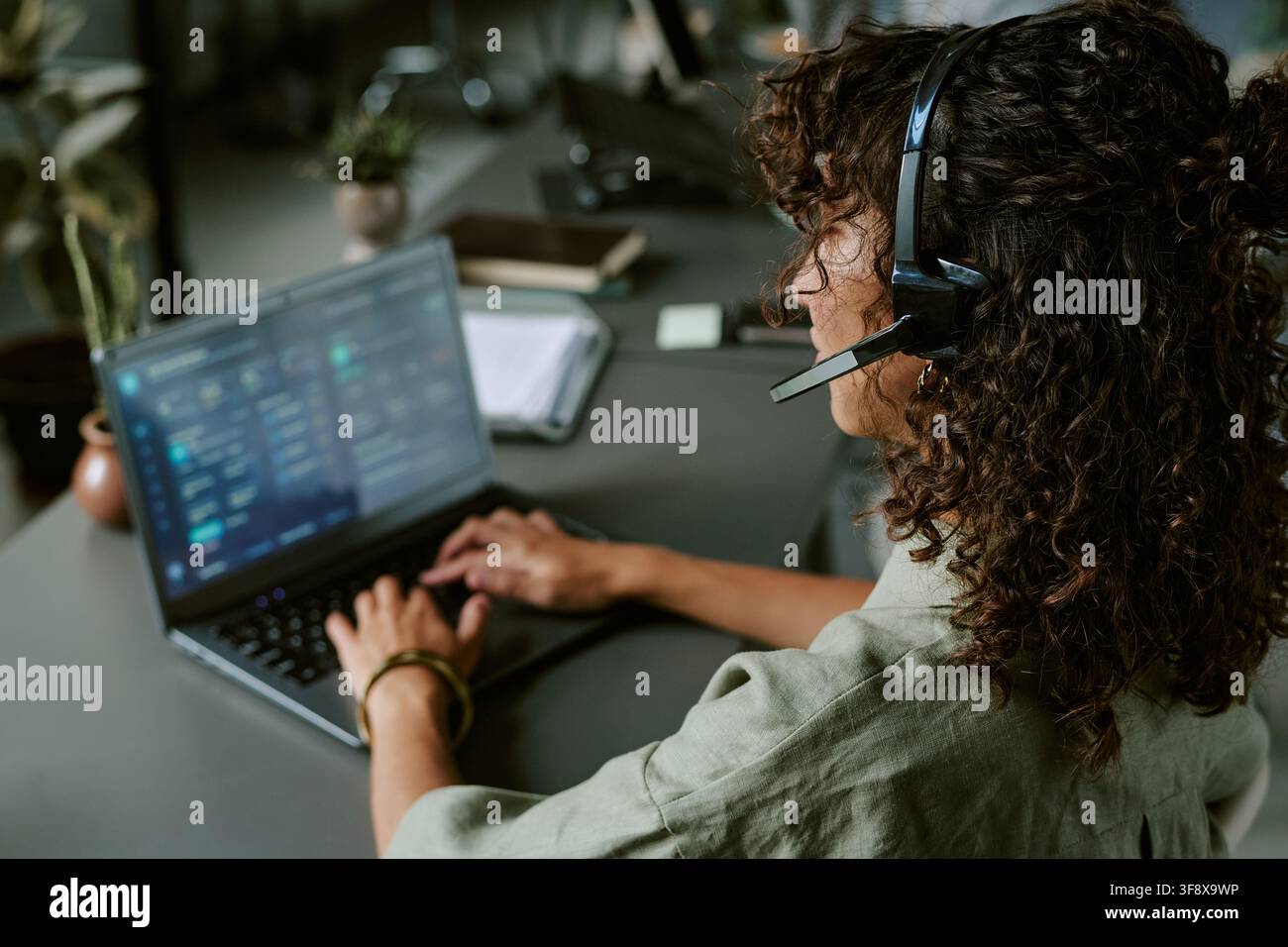Woman Wearing Headset Typing on Laptop in Call Center Stock Photo