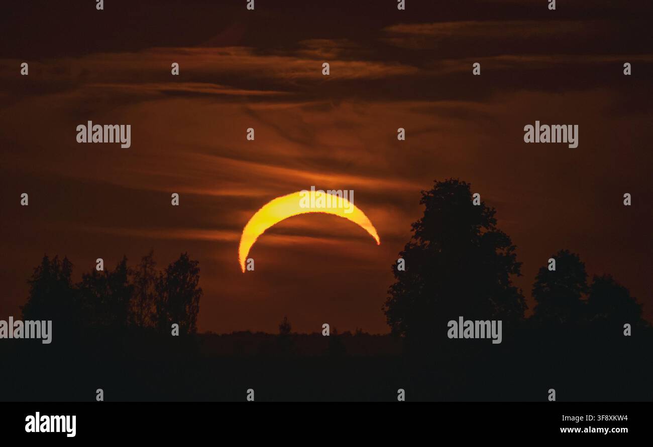 Orange crescent sun during partial solar eclipse in dark sky in Lithuania Stock Photo