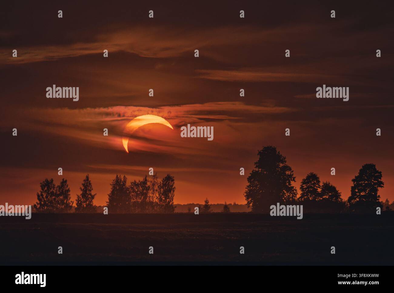 Orange crescent sun during partial solar eclipse in dark sky in Lithuania Stock Photo
