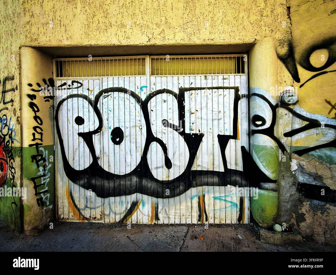 Bold black-and-white graffiti tag reading POST across a weathered garage door and crumbling urban wall Stock Photo