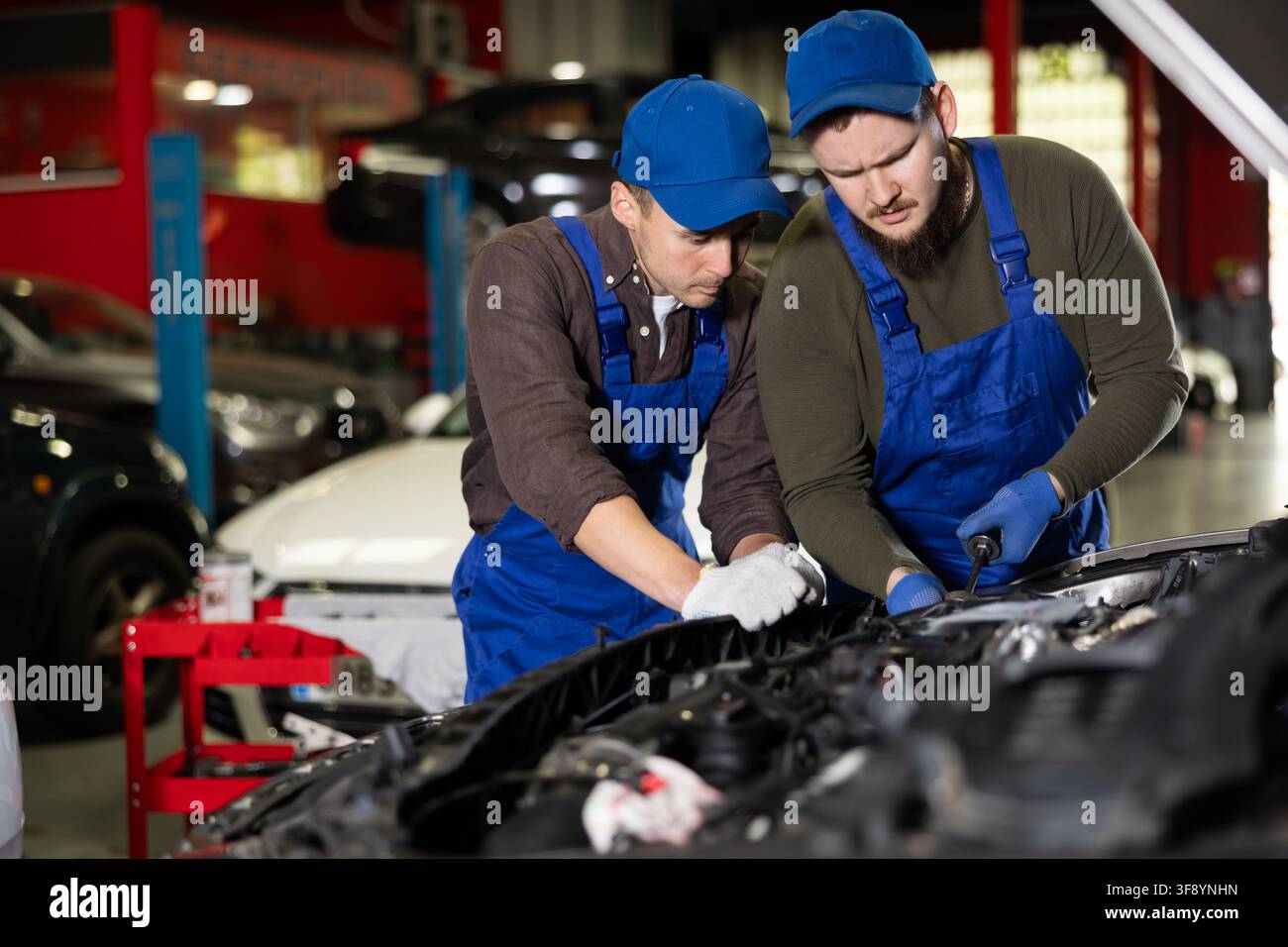 Two professional auto mechanics repairing broken car together in car service center Stock Photo