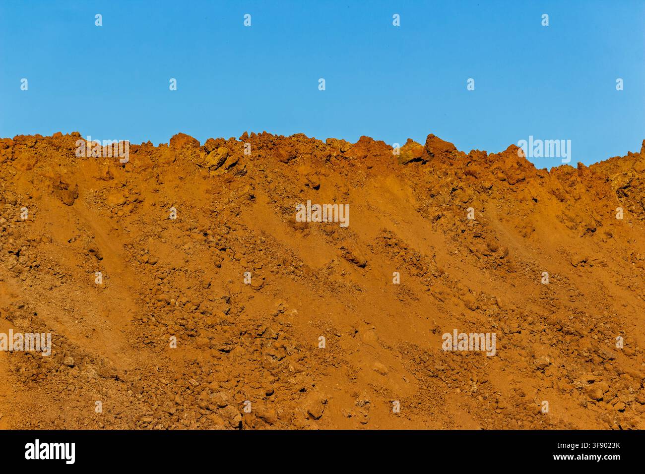 Large heaps of raw soil and dirt piled up at a construction site against a clear blue sky, textured mounds of earth showing excavation progress in bri Stock Photo