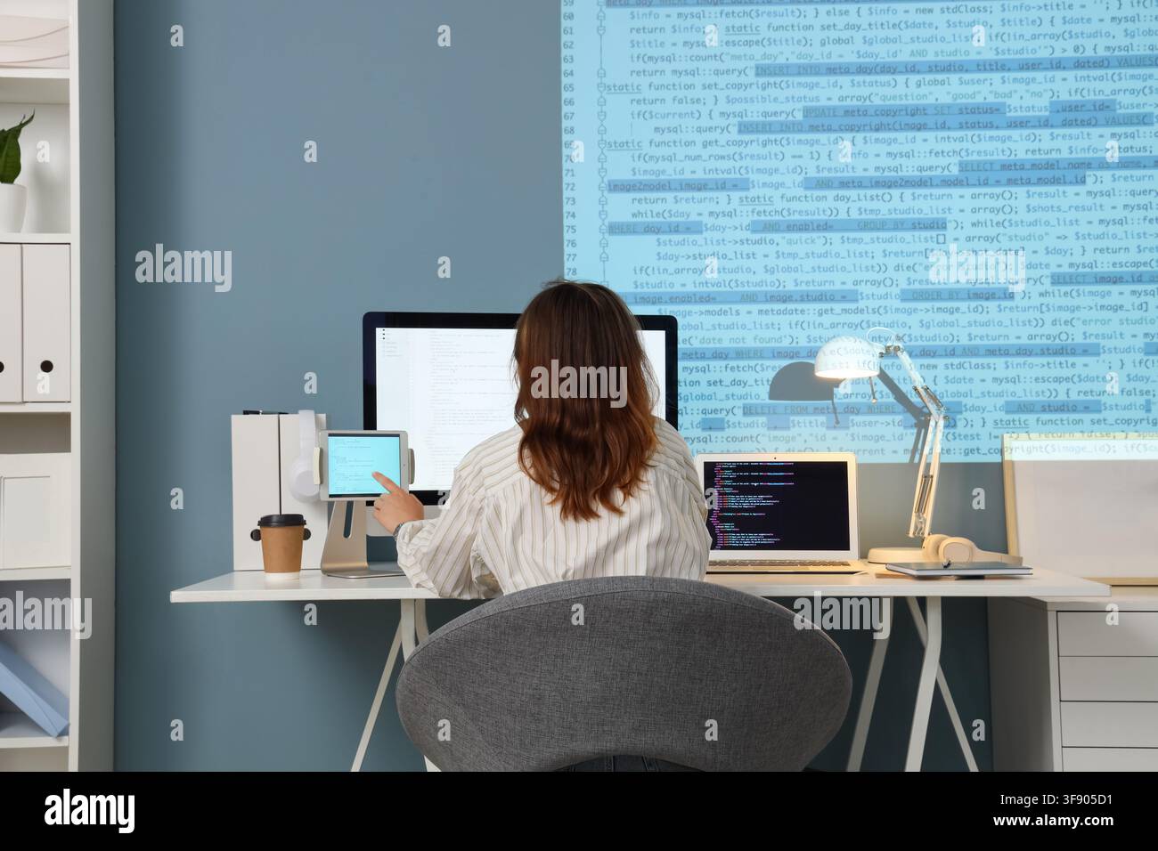 Female programmer working on multiple screens with code displayed, software development and technology Stock Photo