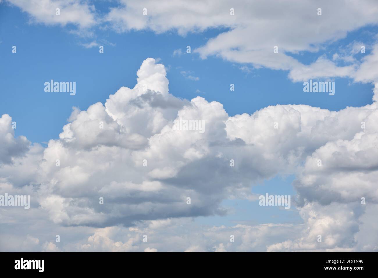 Bright blue sky filled with fluffy white and grey cumulus clouds background on vibrant sunny daylight Stock Photo