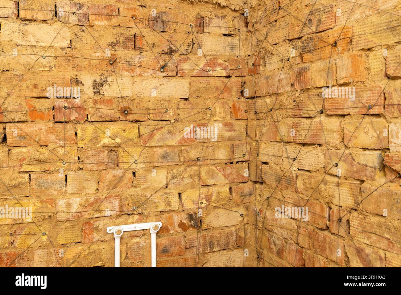 Close-up view of a weathered brick wall featuring a geometric pattern made by thin wires attached to metal fasteners. The bricks display a mix of yell Stock Photo