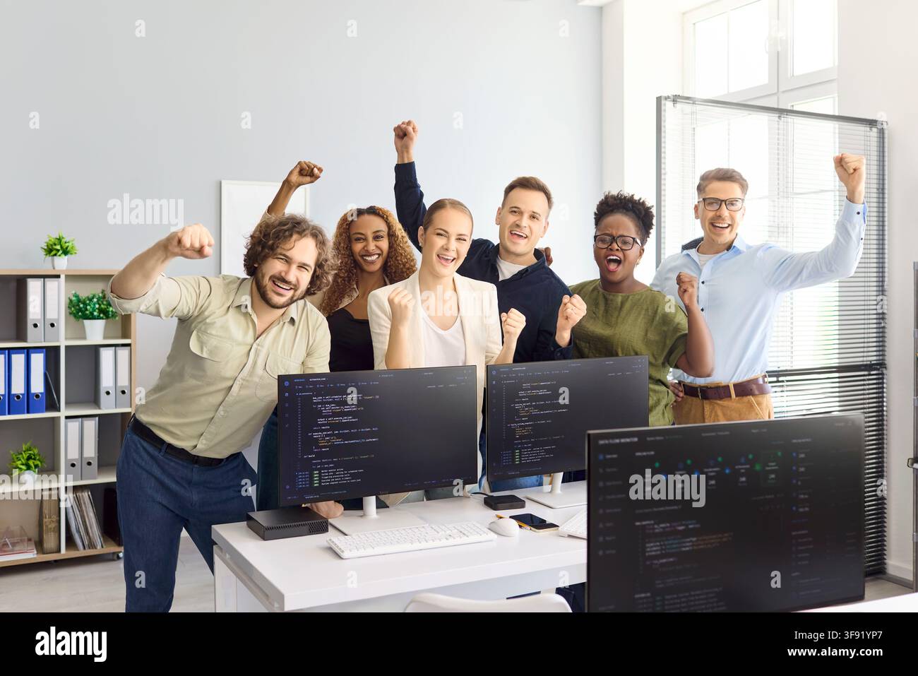Happy diverse developers team cheering in office after coding project success Stock Photo