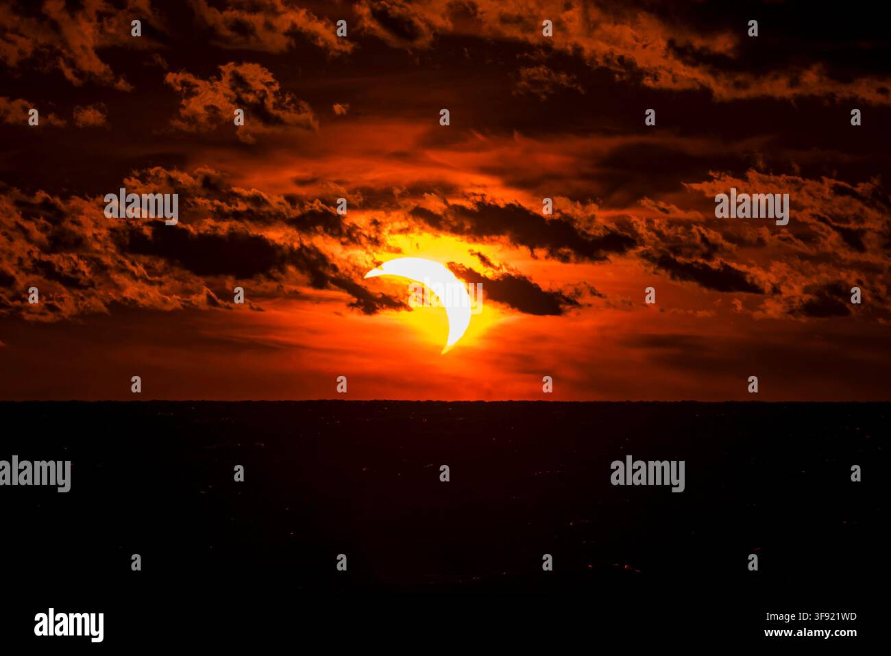 Solar eclipse partially covering the sun during sunset time with dark clouds. Stock Photo