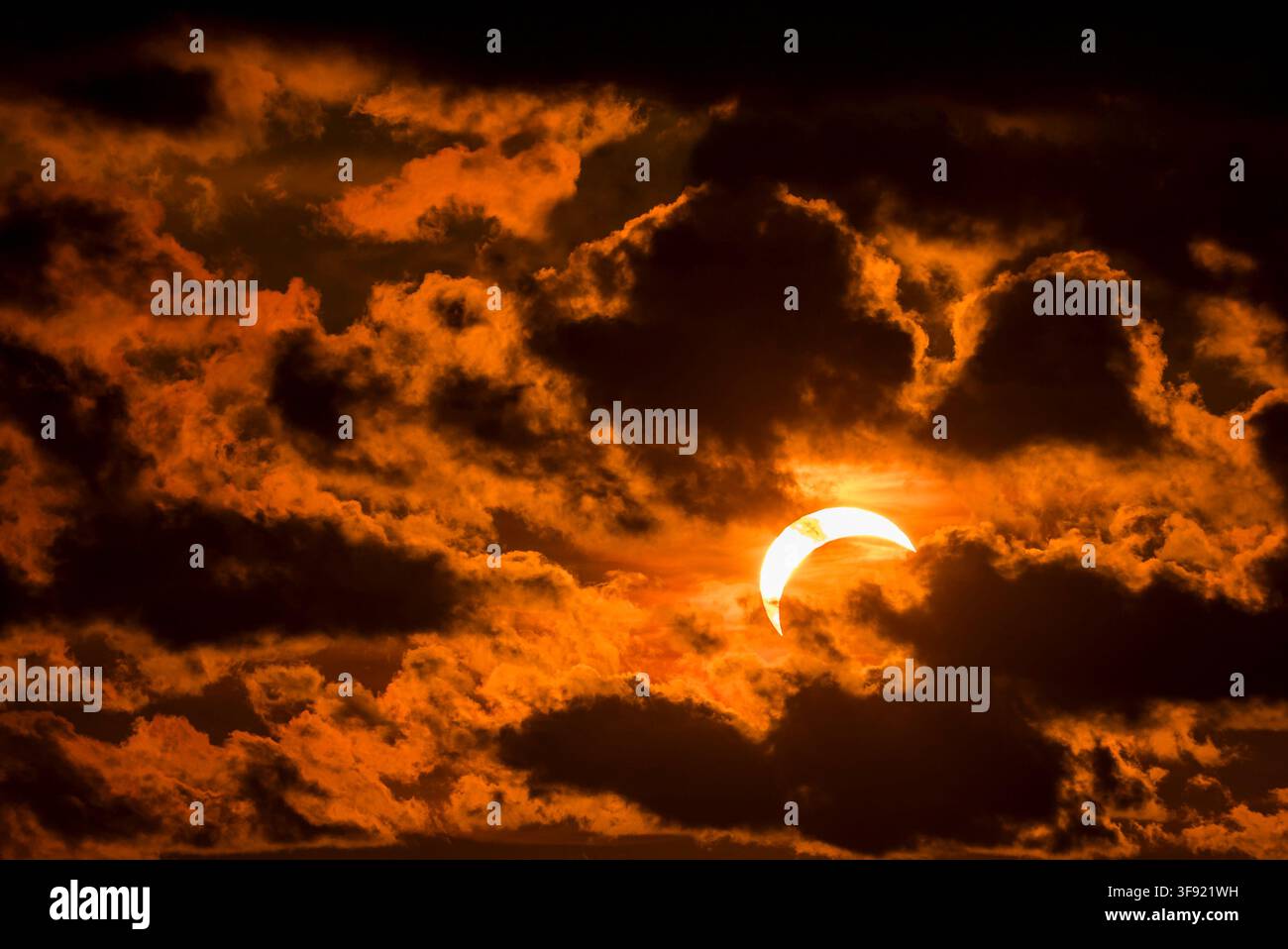 Solar eclipse partially covering the sun during sunset with dark clouds. Stock Photo