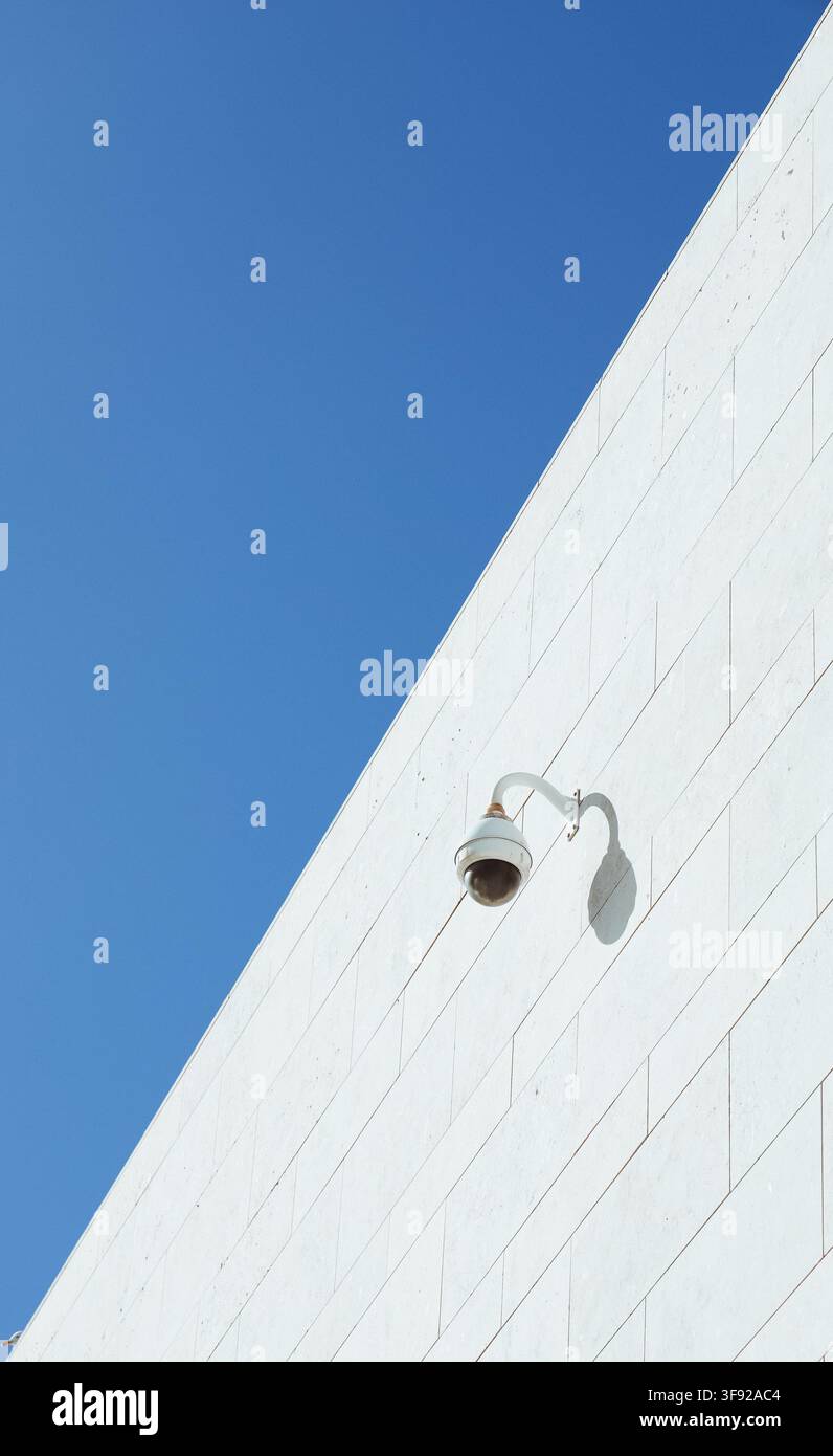 Minimalist security camera on a white wall against blue sky Stock Photo