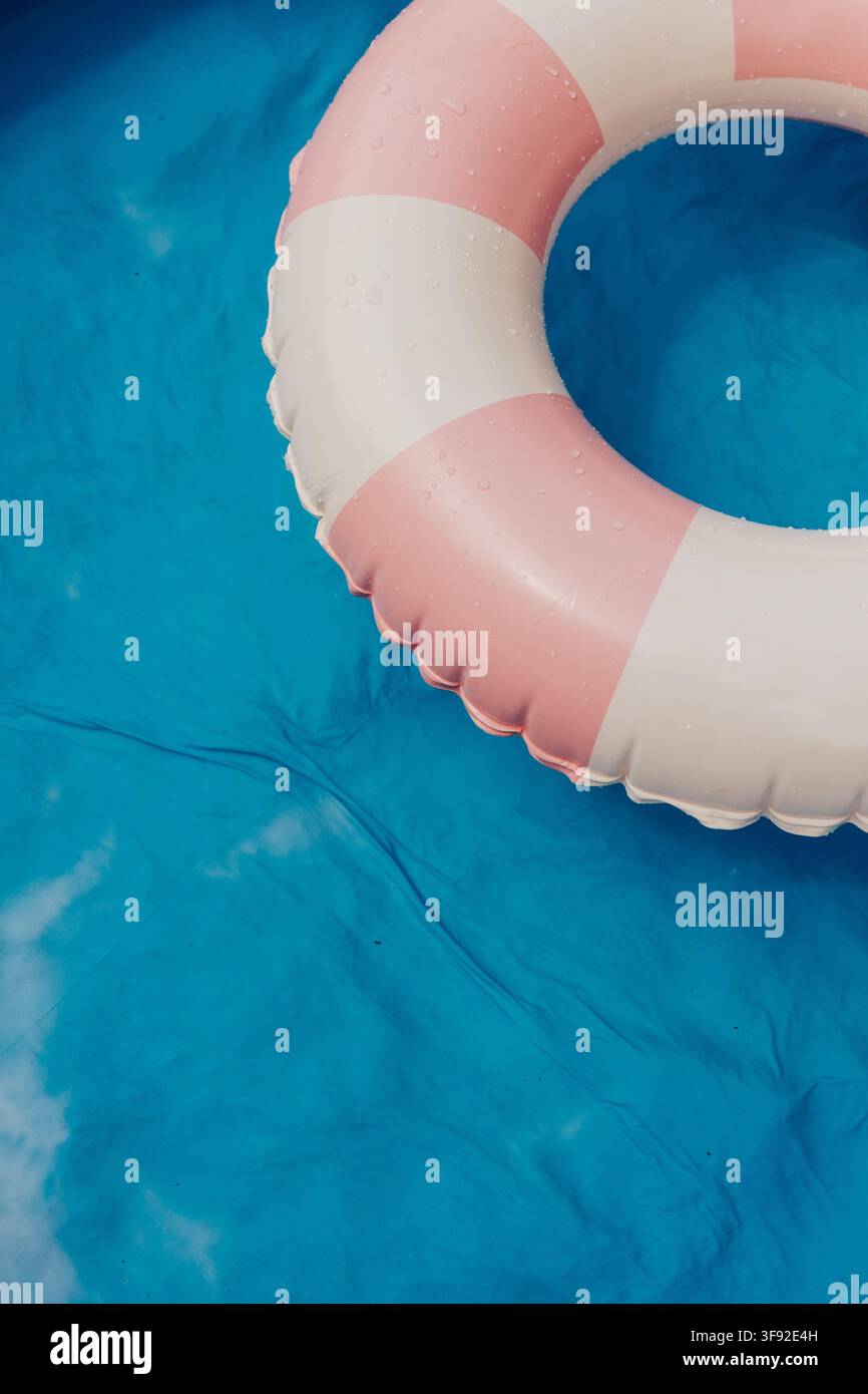 Pink striped inflatable ring floats in blue pool Stock Photo