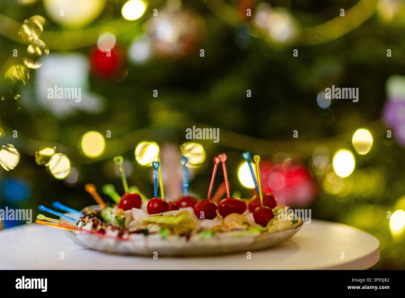 A closeup shot of various colorful appetizers on a plate, set against a festive, blurred background of Christmas tree lights Stock Photo