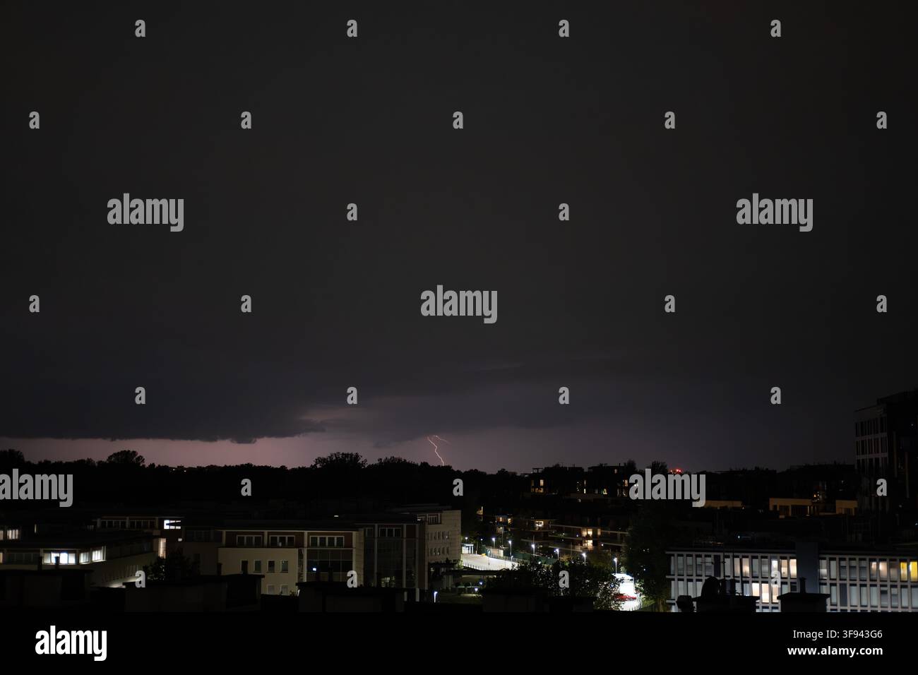 A lightning bolt is striking from dark clouds at a night cityscape. Stock Photo