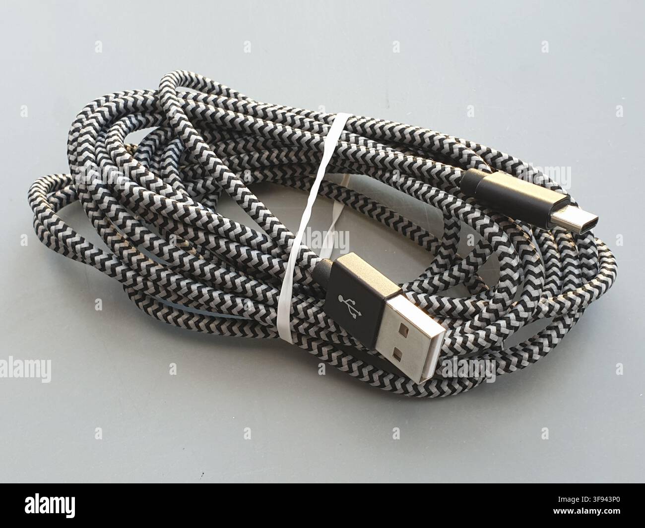 A coiled black and white braided USB cable sits on a grey surface Stock Photo