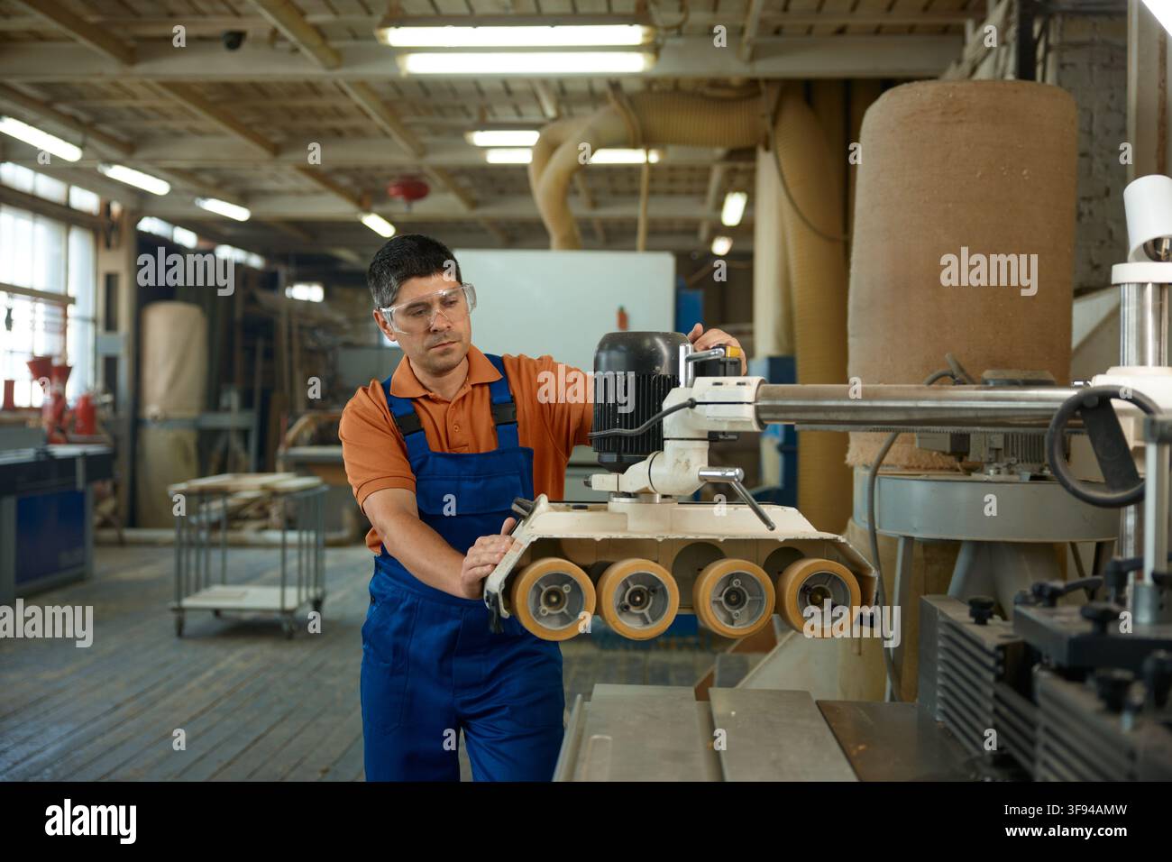 Carpenter adjusting machine settings to ensure consistent thickness and quality of timber Stock Photo