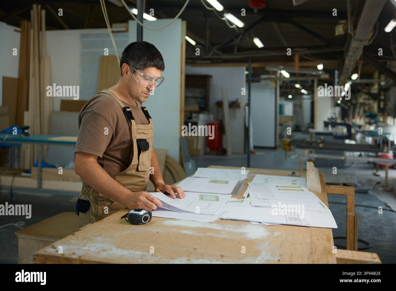 Workman assessing construction drawings in workshop while using measuring instruments and tools Stock Photo