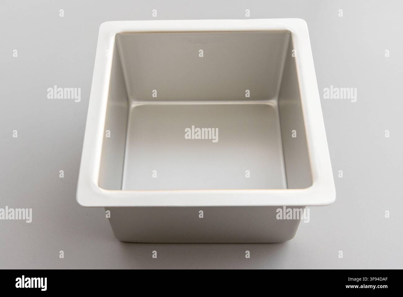 An empty square metal baking pan rests on a plain gray background Stock Photo