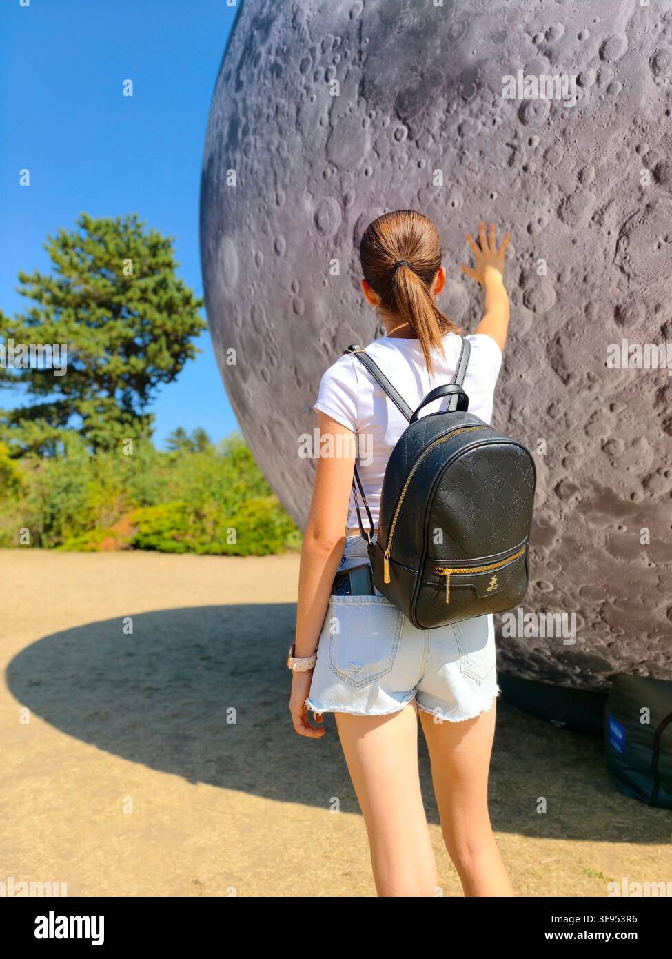 Brno, Czech Republic – August 9, 2026: A young woman visitor touches Lunalon, a giant inflatable model of the Moon, during the final day of the Festiv - Smartphone Captured Stock Image