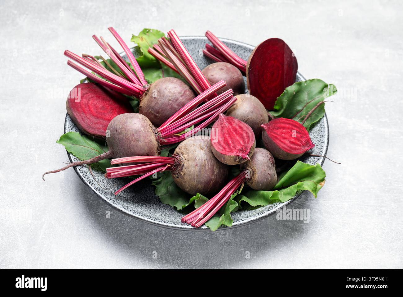 Whole and cut young beets with green leaves on gray textured table, closeup Stock Photo