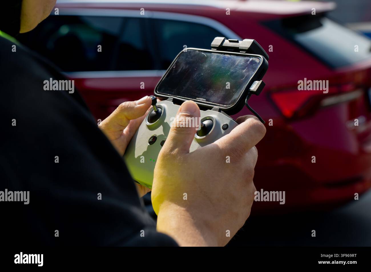 Drone pilot holding remote controller with connected mobile device displaying flight interface representing aerial surveying and control Stock Photo
