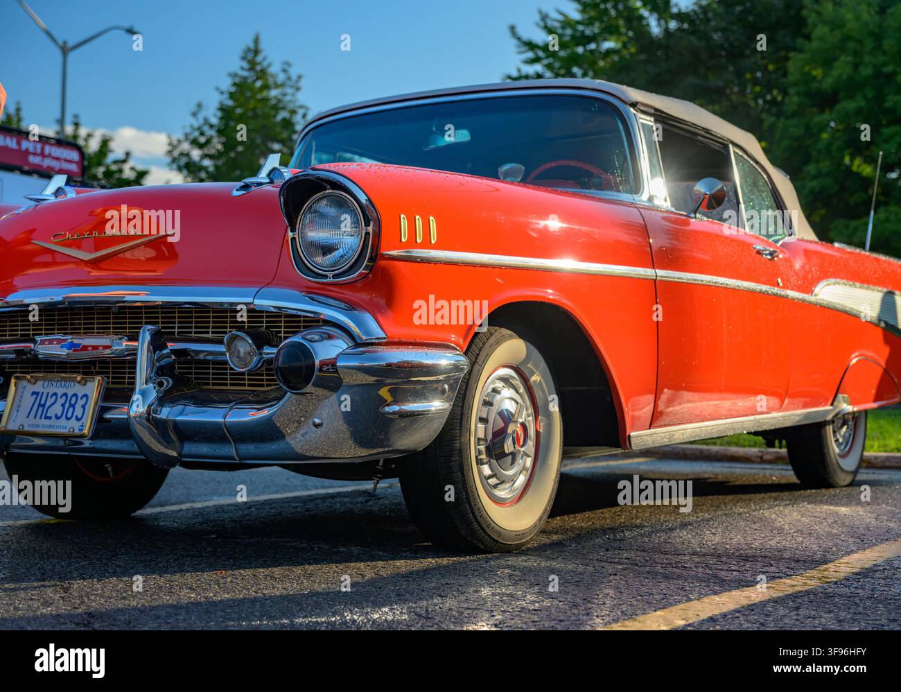 A low-angle front view of a classic red 1957 Chevrolet Bel Air convertible featuring shiny chrome trim, whitewall tires, and an Ontario license plate. Stock Photo