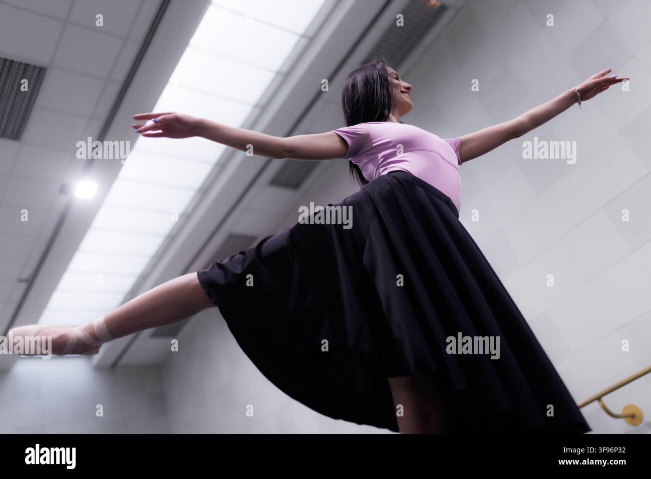 Ballet dancer practices in a studio with large windows and bright lighting during daytime Stock Photo