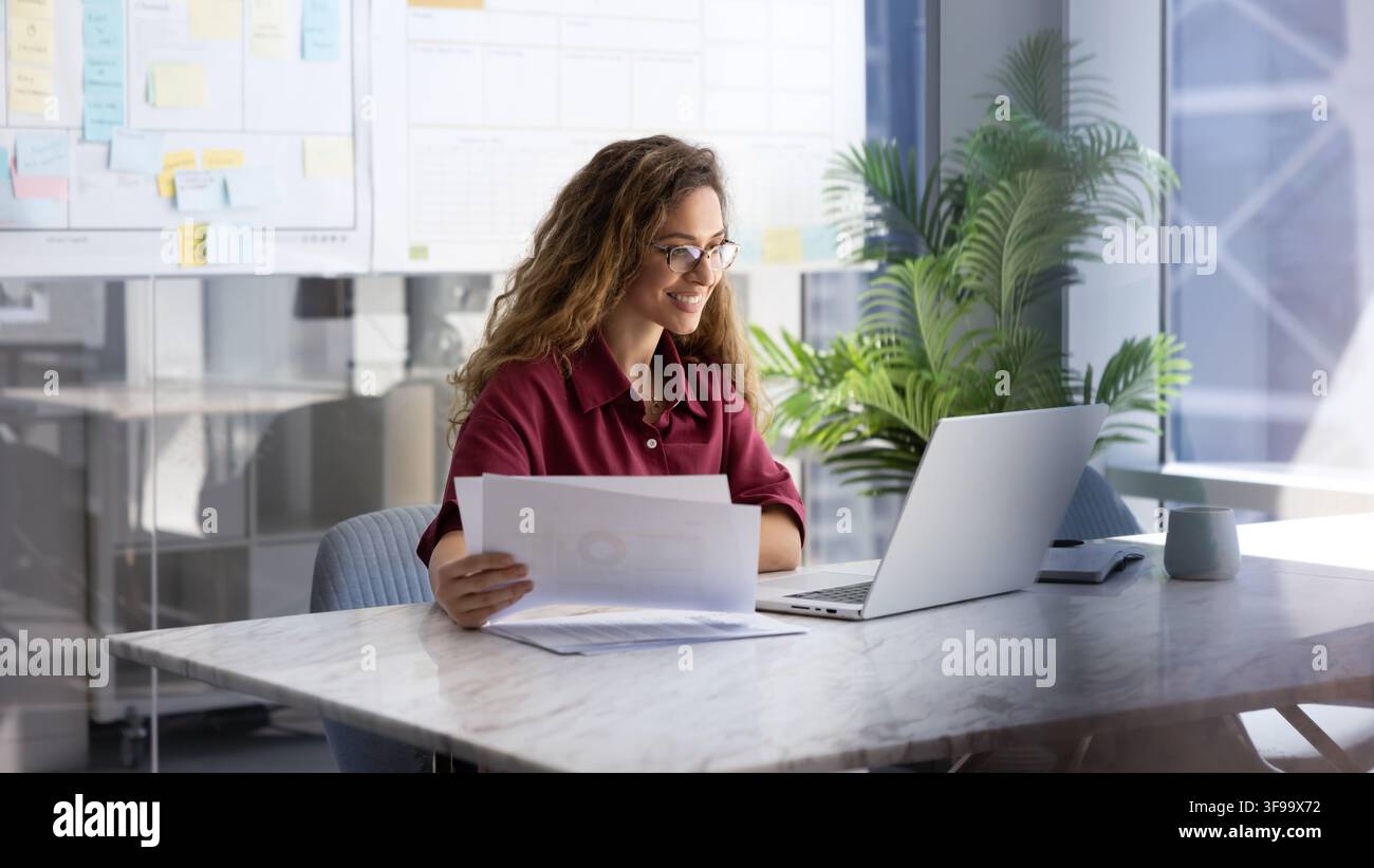 Businesswoman reviewing documents at workplace desk with laptop Stock Photo