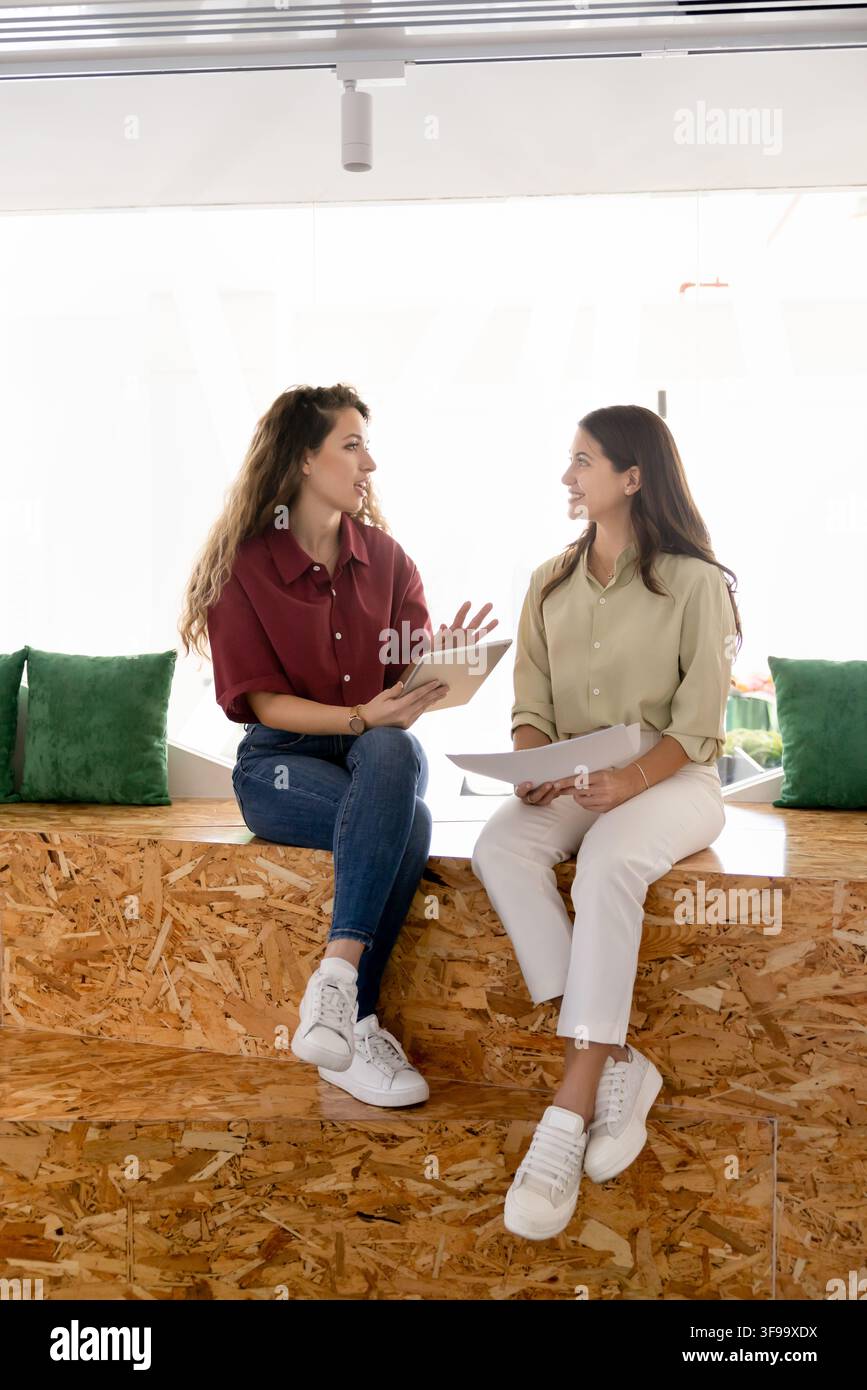 Women coworkers discussing project, or documents details in coworking Stock Photo