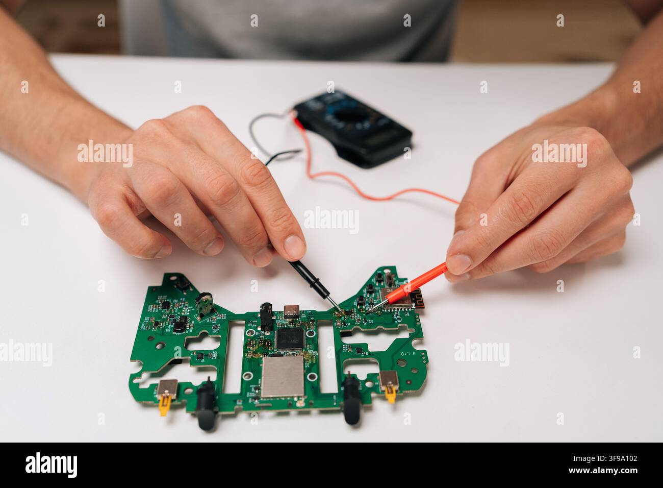 Repairman hands troubleshooting game controller circuit board with multimeter, checking electronic components and diagnosing potential issues during Stock Photo