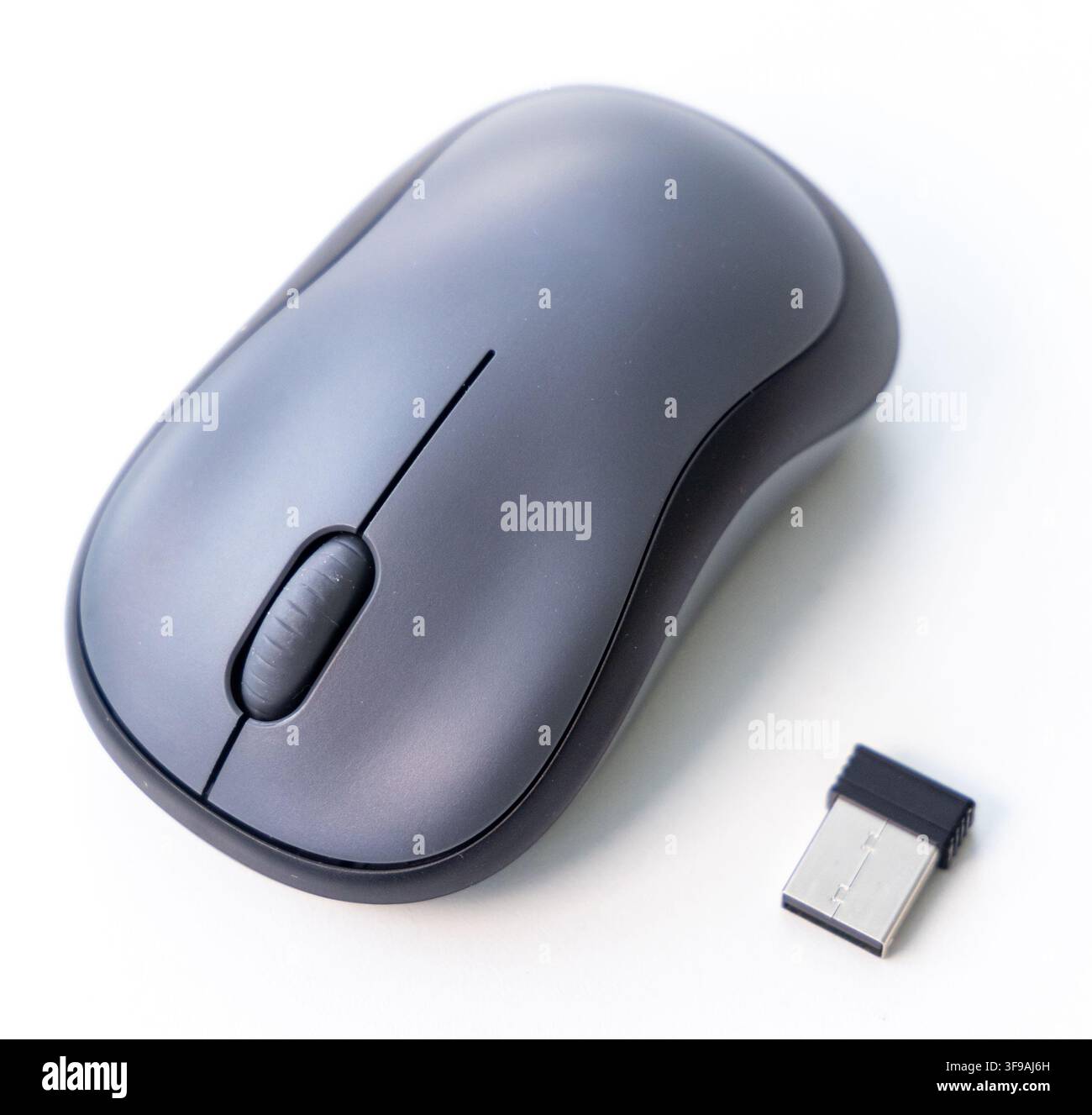 A gray wireless mouse and USB receiver are on a white surface Stock Photo